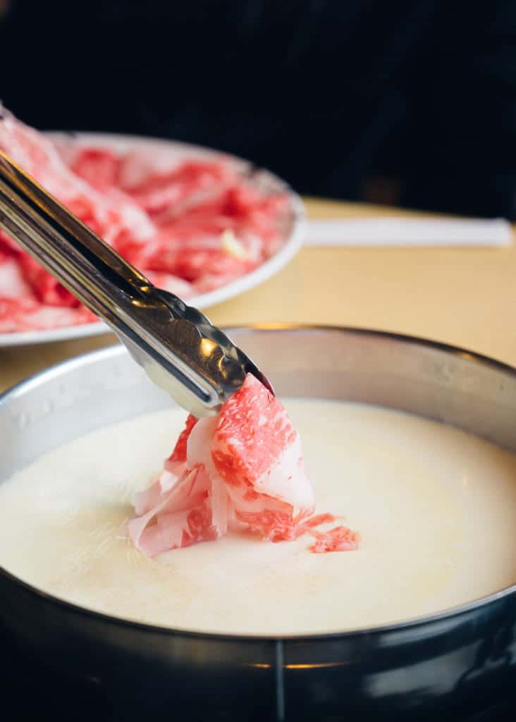 tongs holding shabu shabu and dipping to sauce in japa
