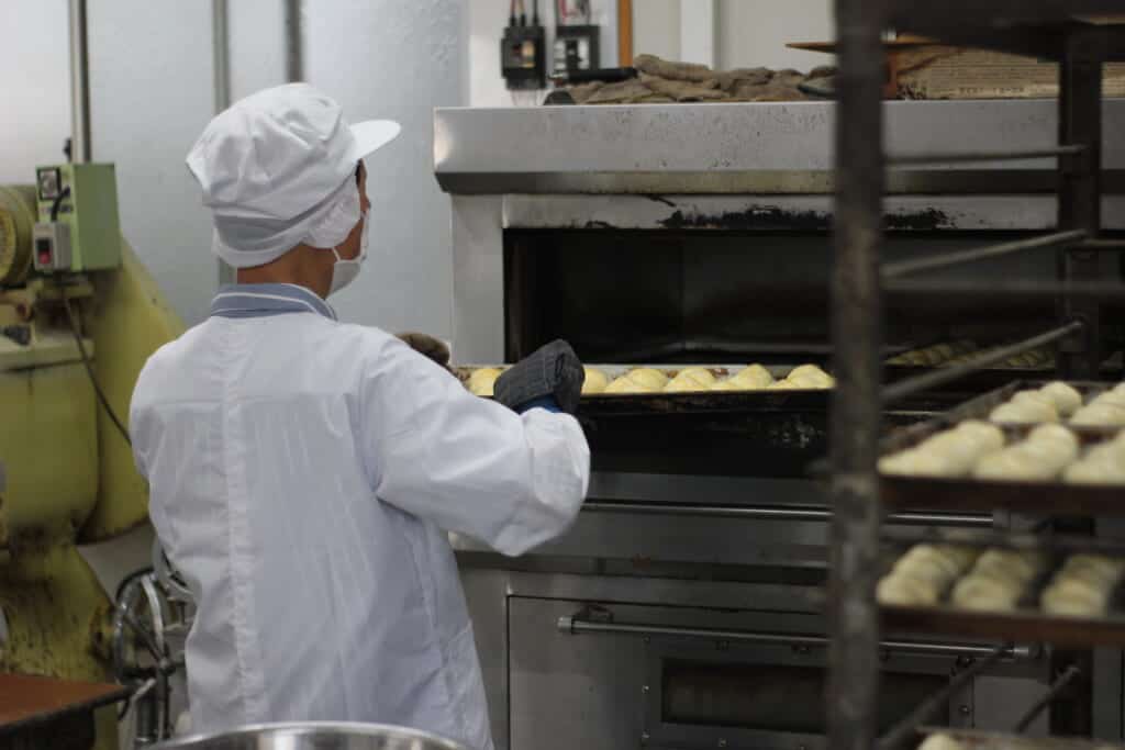 A man putting a tray full of Japanese pastries in an over