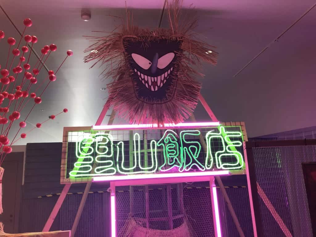 An artwork showing a pink frightening character and a green neon sign