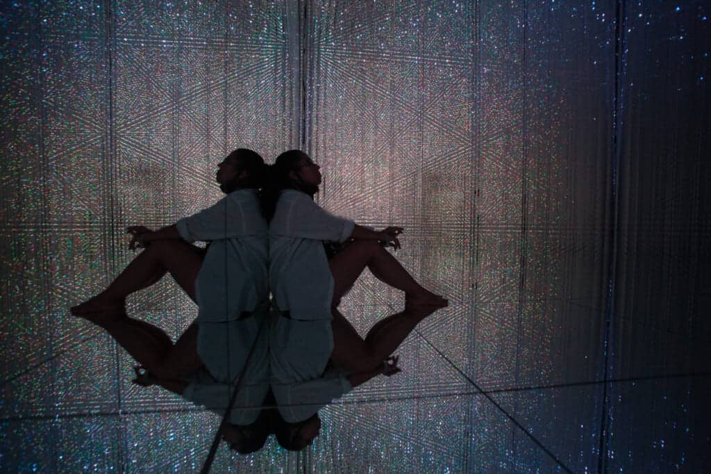 woman sitting in the mirrored floor surrounded by crystals of light at teamLab Planets in Tokyo