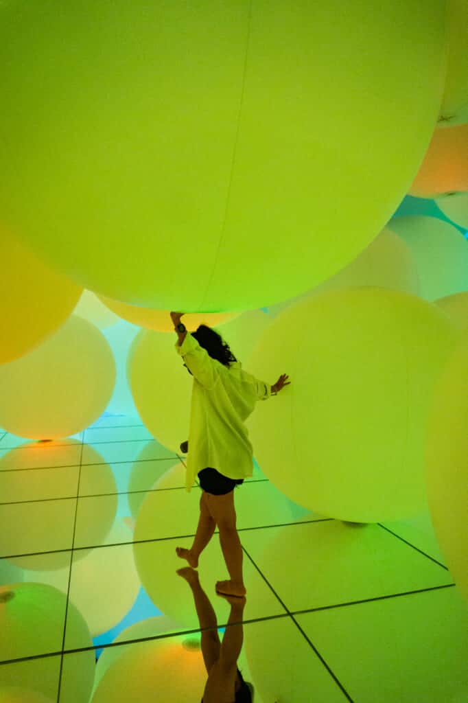 woman wandering around yellow spheres of light at teamLab Planets in Tokyo