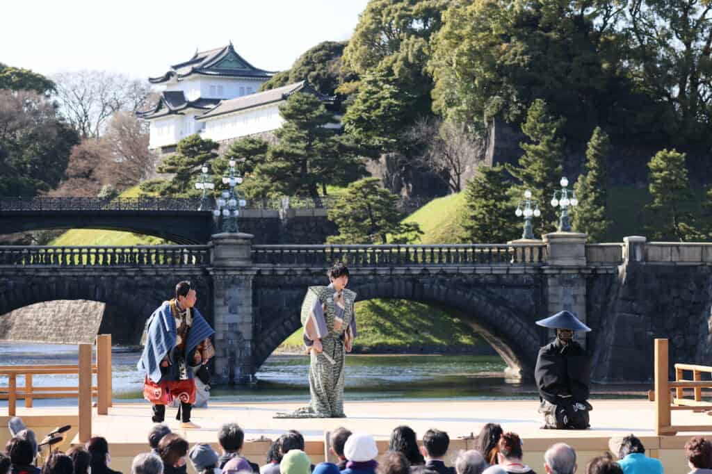 Traditional Japanese Kyogen Noh performers on stage in front of bridge and palace in Japan