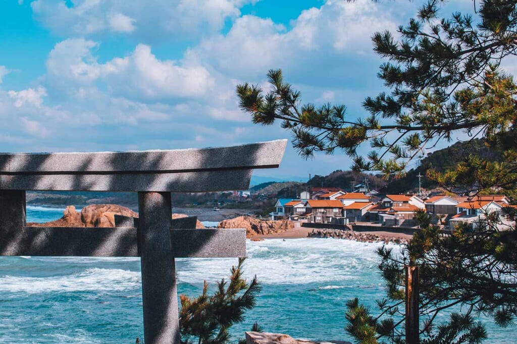 View of the Japanese coastline and orange roofs with part of a Torii gate in the foreground