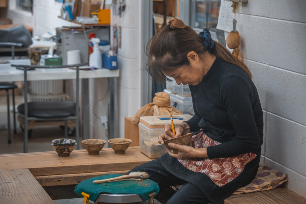 a craftswoman decorating japanese pottery in Okinawa, Japan