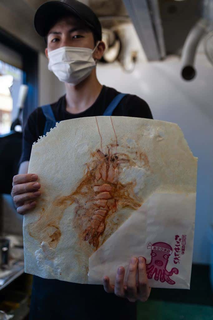 man holding fresh-grilled shrimp rice cracker