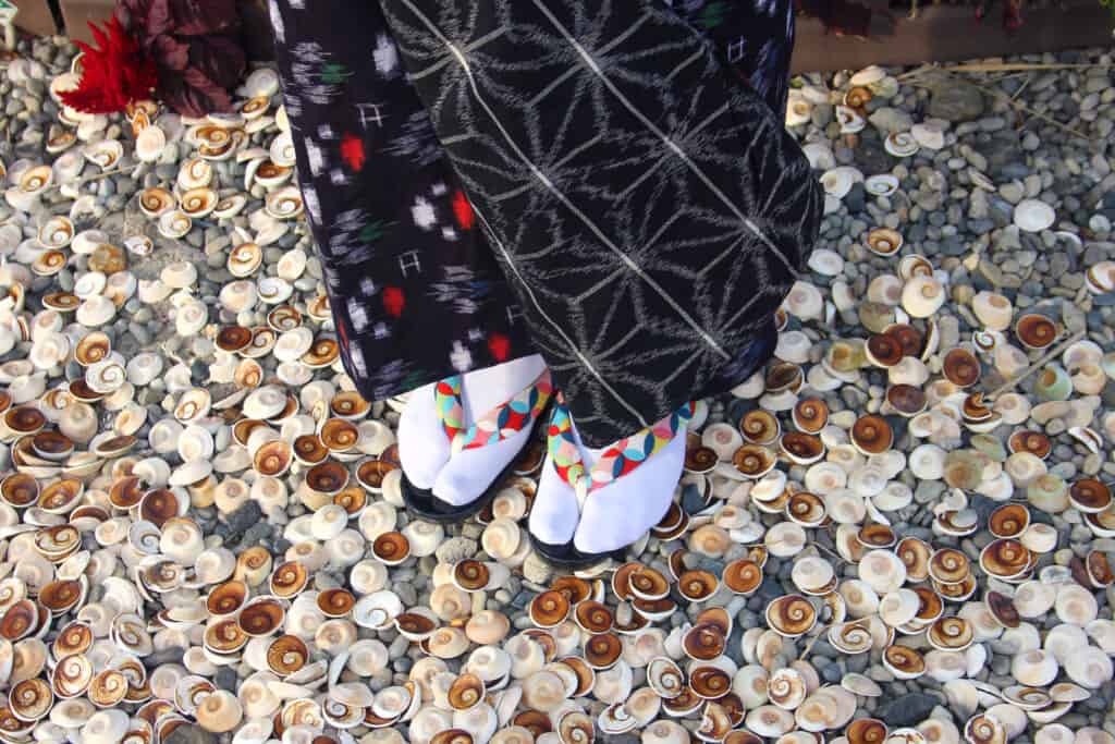 Someone is standing on a floor covered by sea shells, we only see the foot of the person and the bottom of her skirt