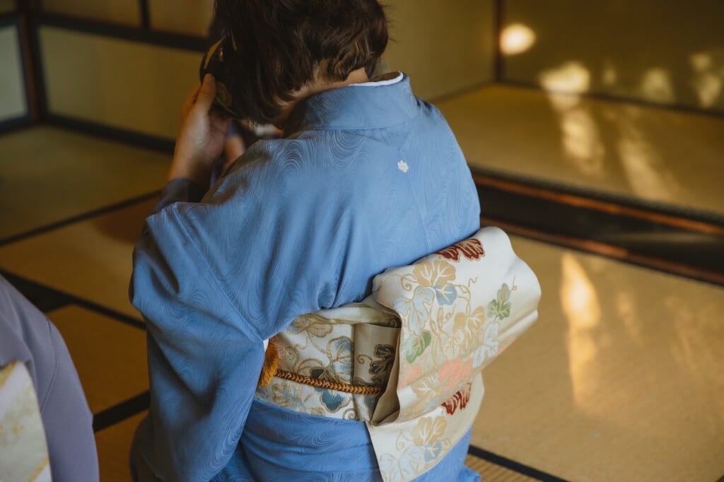 A woman dressed in a blue iromuji kimono drinks from a chawan during the tea ceremony.