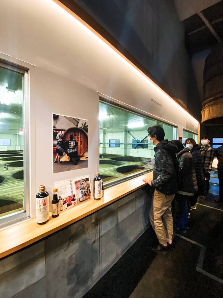 man looking through display window into a large soy sauce brewery