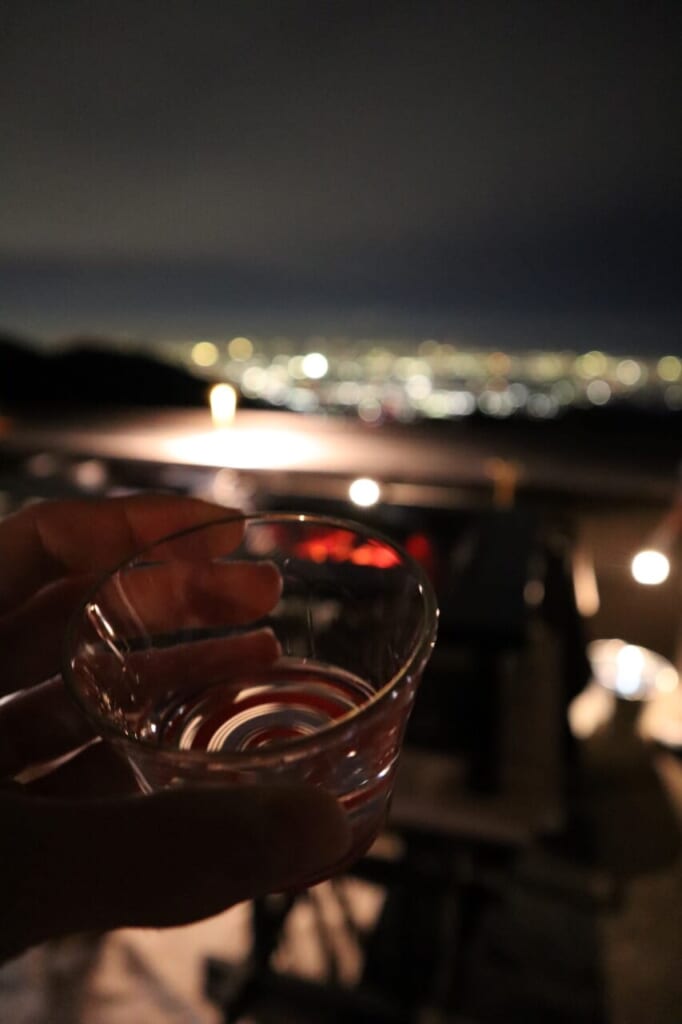 hand holding glass in front of night cityscape view from mountain