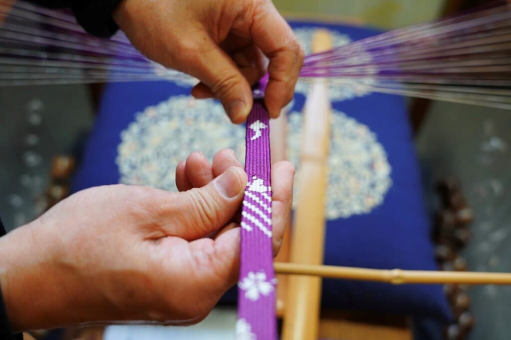 A gentleman's hands holding a piece of kumihimo on a traditional craft tool