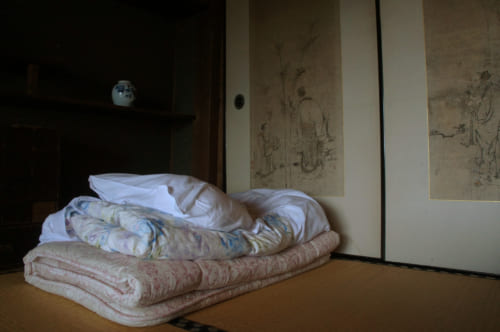Futon plié, posé sur les tatamis devant des parois peintes à l'encre