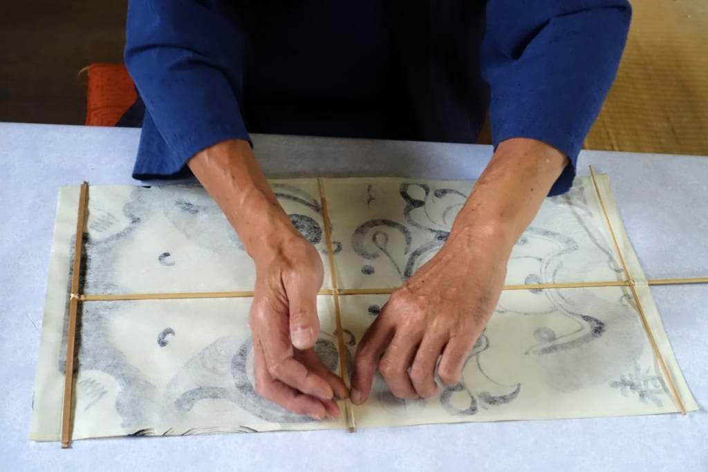 L'artisan place minutieusement l'armature en bambou du cerf-volant sur le papier peint à la main