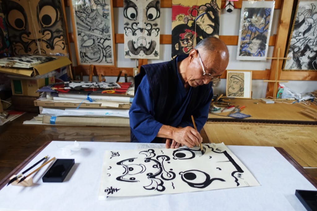 Un artisan peint les contours d'un personnage sur un cerf-volant traditionnel dans son atelier à Yuzawa, préfecture d'Akita
