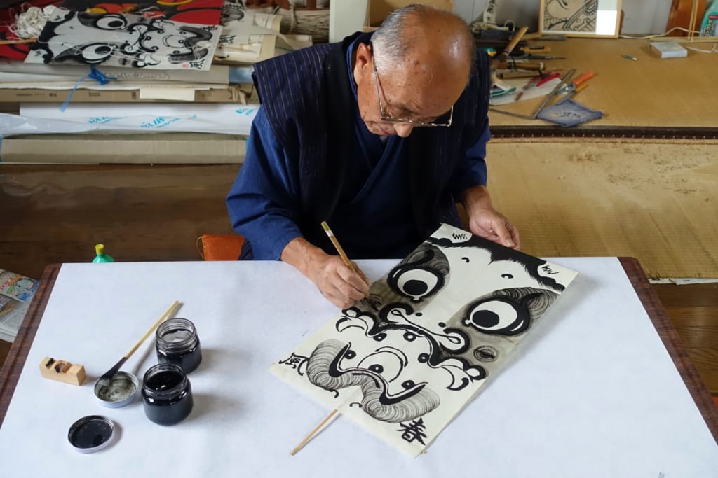M. Ono, dessinant avec soin le motif de son cerf-volant à l'encre noire