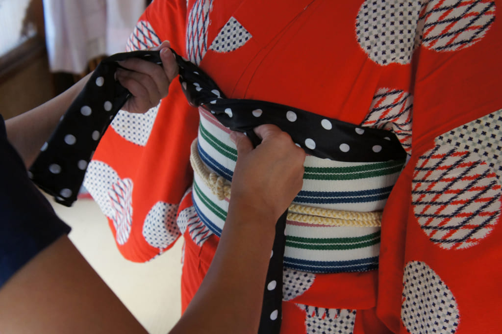 Risa nouant un obi-age noir à pois blancs au-dessus de l'obi