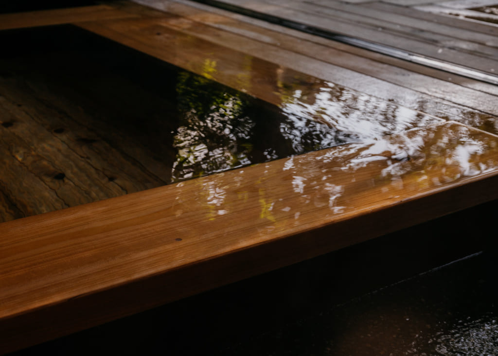 Eau de l'onsen, recouvrant les bords du bassin et reflétant les arbres