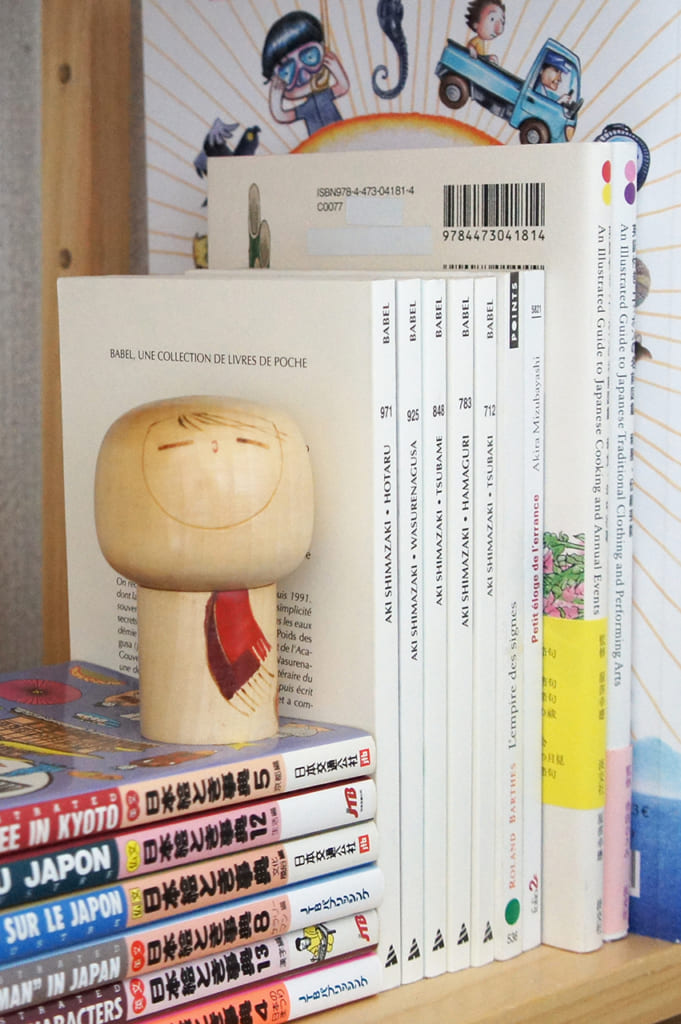 Kokeshi créative avec écharpe devant une sélection de livres sur le Japon