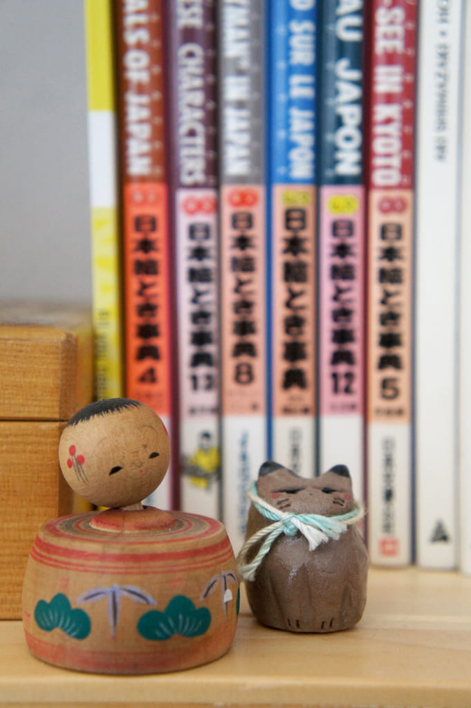 Petite kokeshi et chat en céramique devant des livres