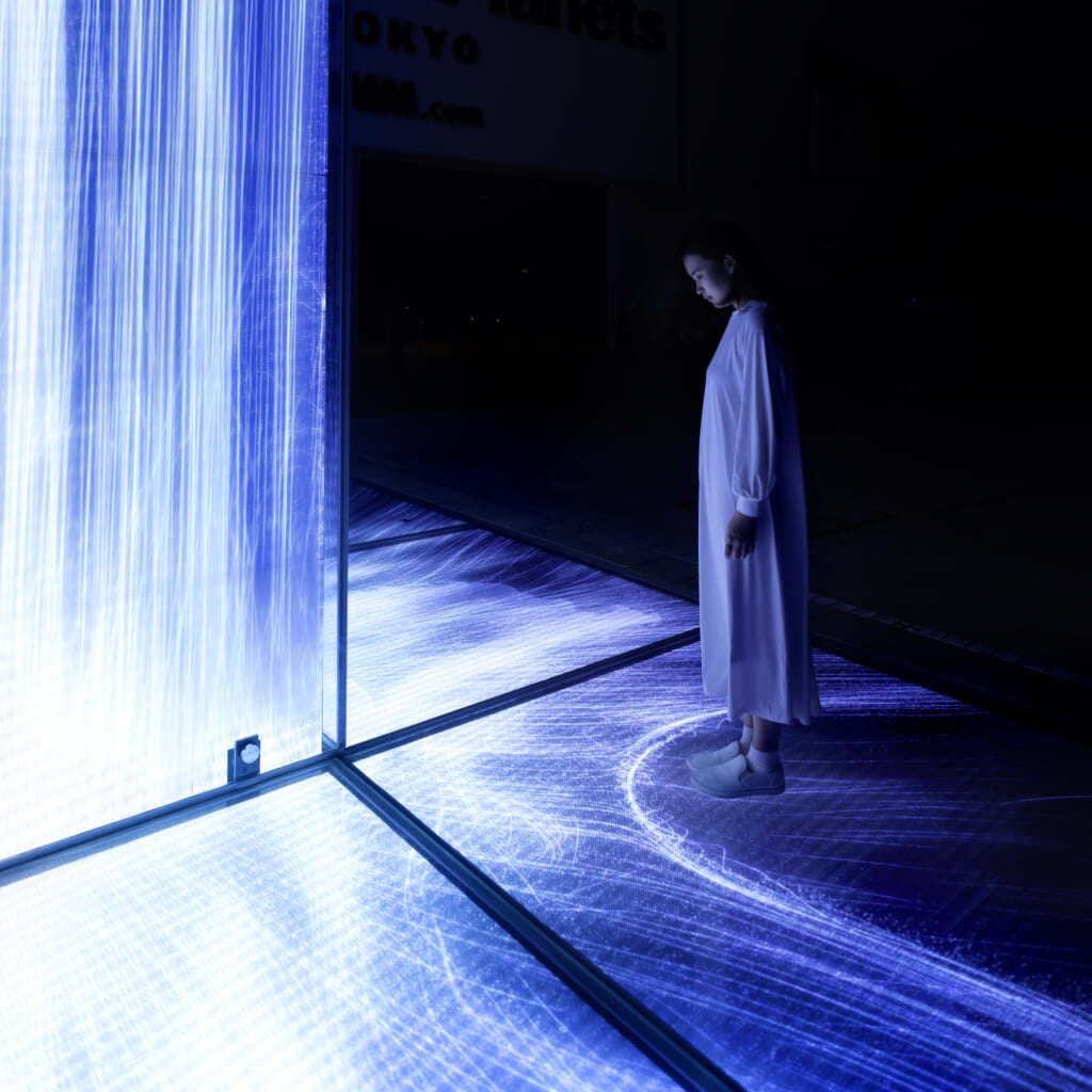 Une femme devant l'oeuvre digitale Universe of Water Particles Falling from the Sky