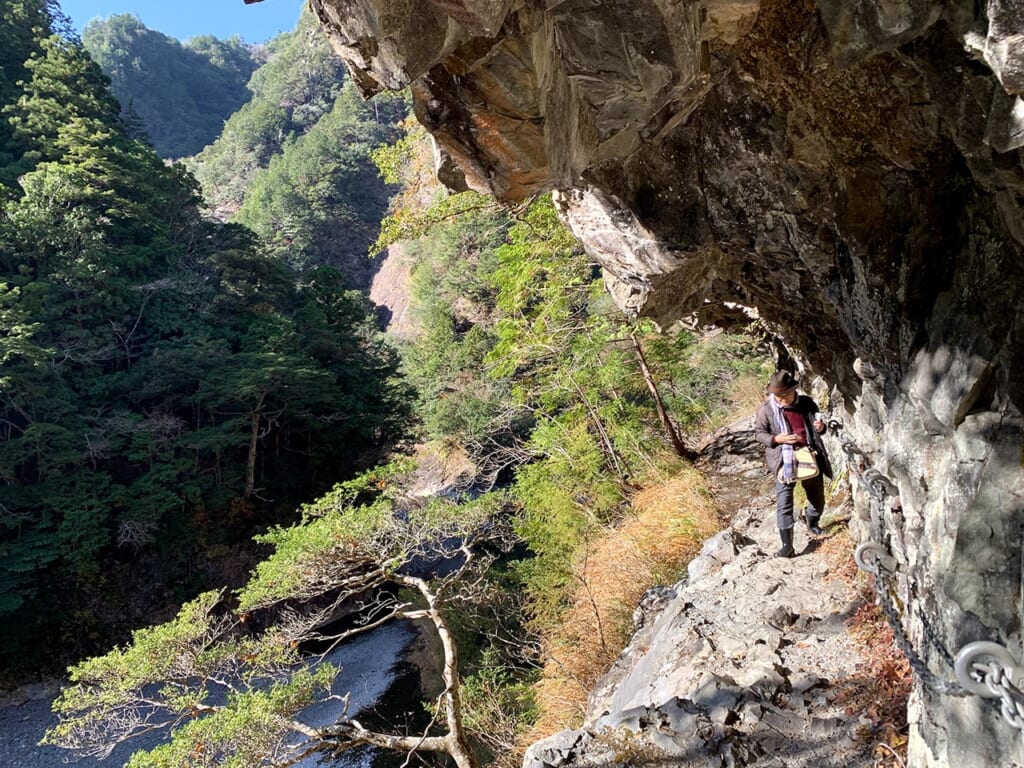 Homme marchant sur un sentier de montagne à flanc de montagne, en se tenant à une chaîne