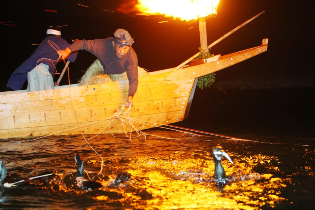 Japonais pratiquand la pêche traditionnelle au cormoran la nuit, à la lumière d'un feu