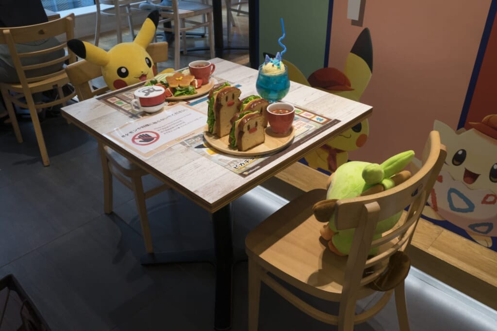 Pokémon installés à une table du Pokémon Café, devant des répliques de plats en plastique