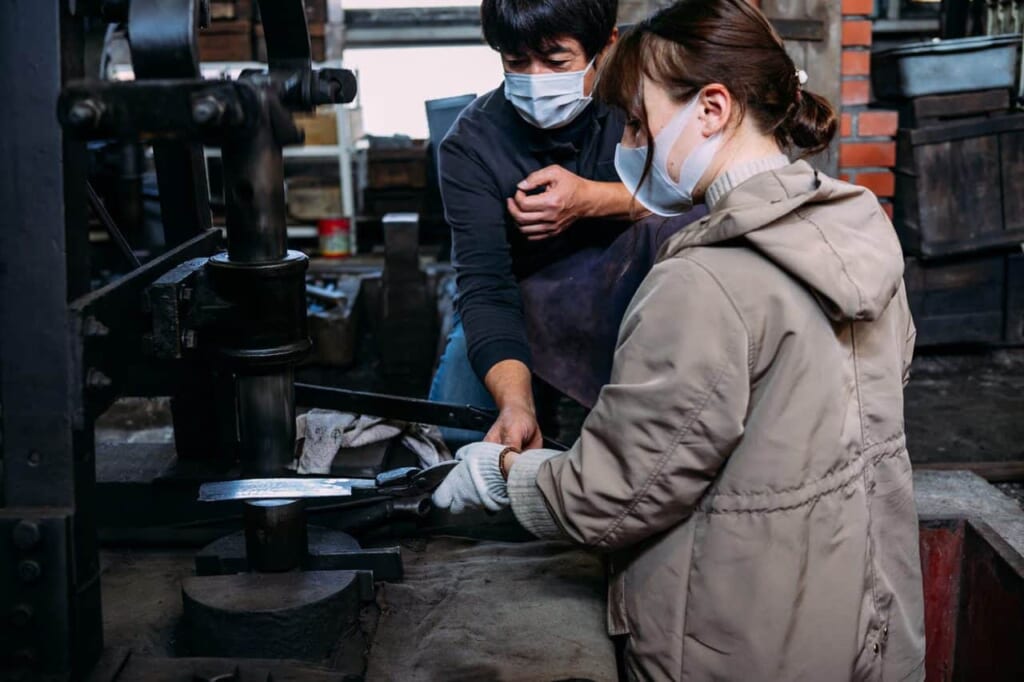 un artisan apprend à une touriste à forger un couteau japonais