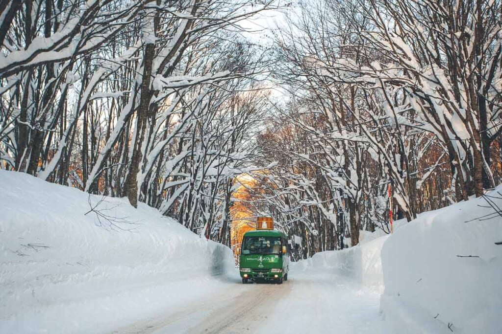Un bus japonais surmonté d'un bain onsen roulant sur une route enneigée