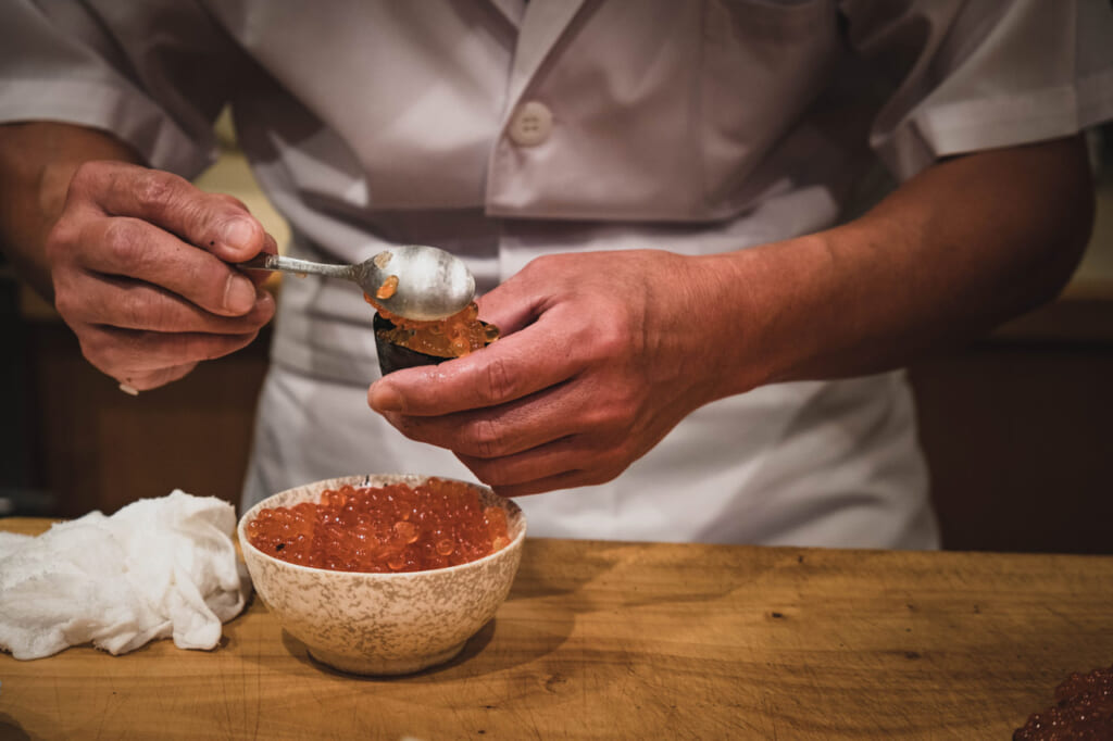 Un maître sushi japonais prépare un maki sushi au œufs de saumon