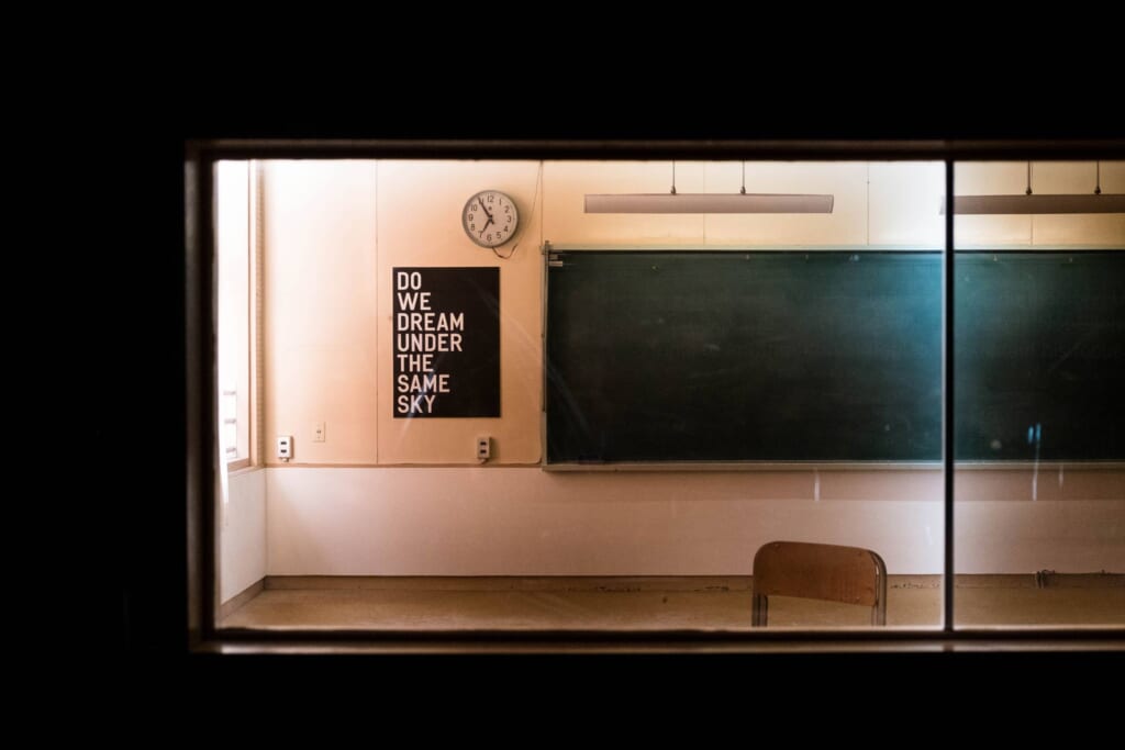 Installation d'Apichatpong Weerasethakul dans une salle de classe désaffectée avec un poster du slogan d'Okayama Art Summit 2022 "Do We Dream Under The Same Sky"