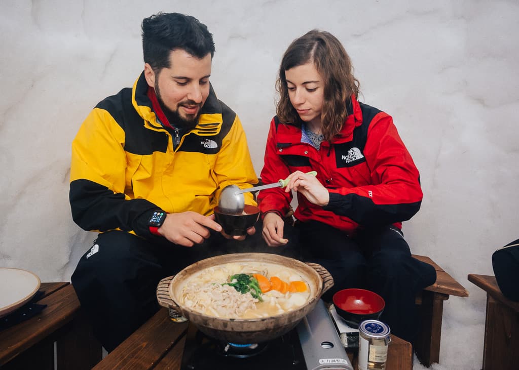 María sirviendo a Hernán su bol de nabe dentro del iglú